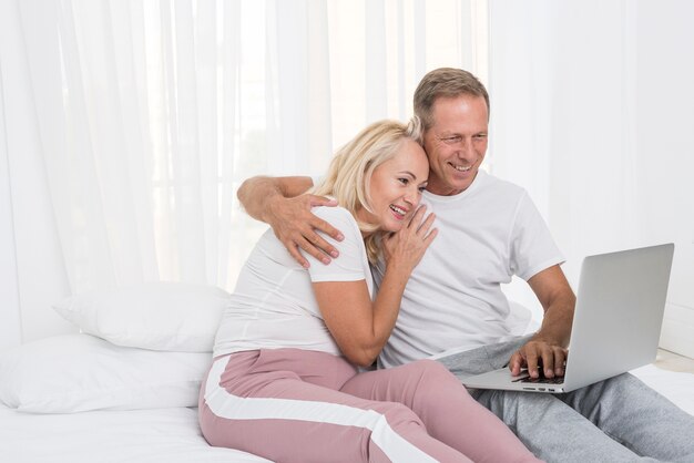 Middelgroot geschoten gelukkig paar met laptop in de slaapkamer