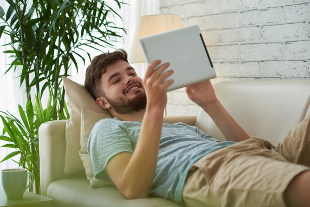 Middelgroot schot van de jonge mens die zijn vrije tijd doorbrengt die ebook op zijn digitale tablet lezen