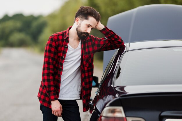 Middelgroot schot van de mens die op auto leunt