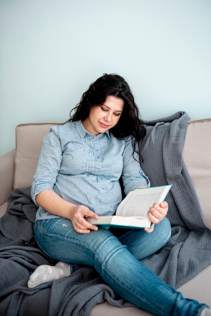 Middelgroot schot zwangere vrouw die een boek leest