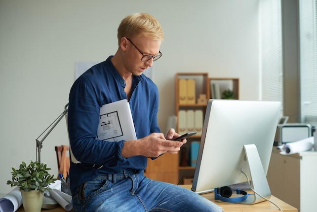 Middelgrote close-up van de blonde mens die aan cliënt texting die op het bureau neerstrijkt