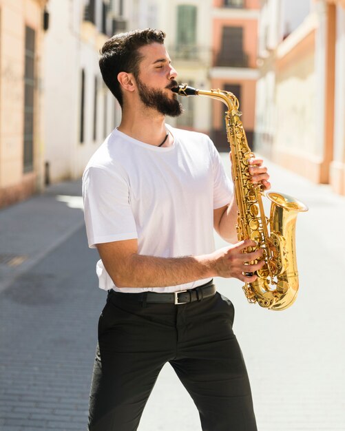 Middelgrote geschotene vooraanzichtmusicus het spelen saxofoon in straat