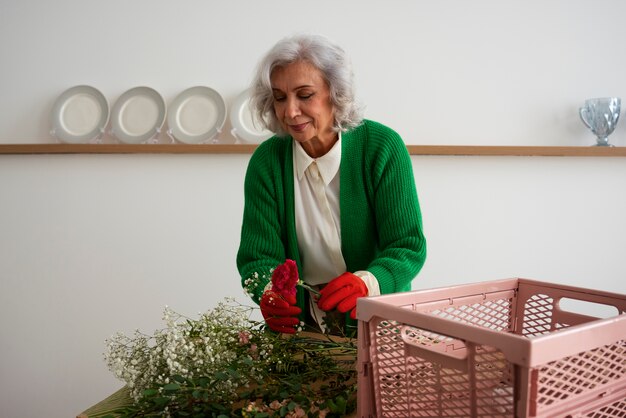 Middelgrote oude vrouw die voor planten zorgt.