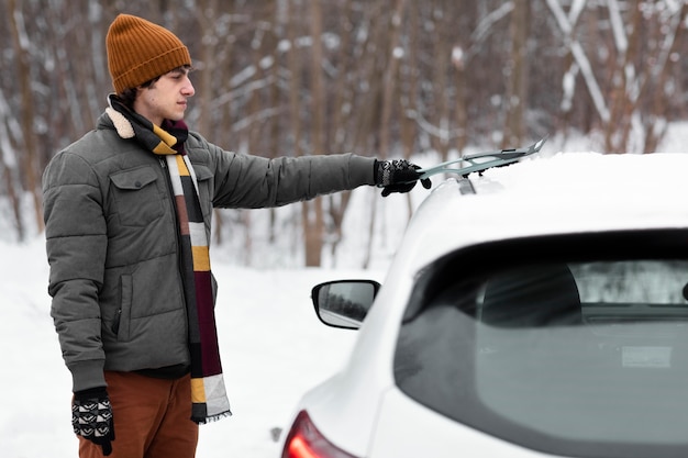 Gratis foto middellange geschoten man die sneeuw uit de auto verwijdert