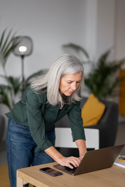 Middellange geschoten oude vrouw die thuis aan laptop werkt