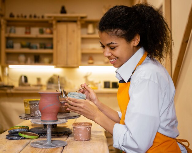 Middellange geschoten smileyvrouw die kleipot schildert