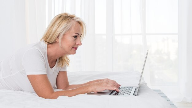 Middellange geschotene blondevrouw in bed met laptop