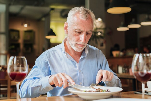 Middellange geschotene oude mens die bij restaurant eet