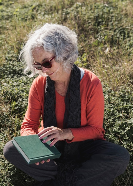 Middellange geschotene oude vrouw met boek in openlucht