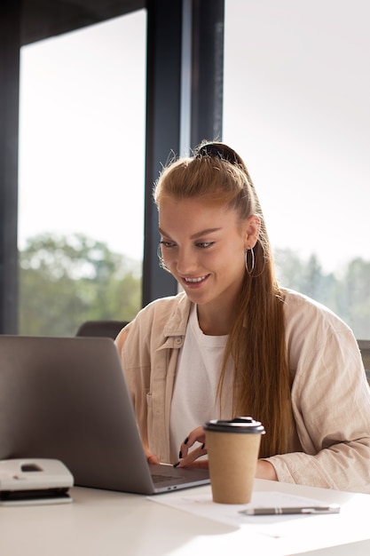 Middellange geschotene smileyvrouw die aan laptop werkt