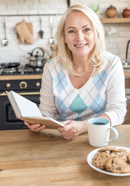 Middellange geschotene smileyvrouw met boek in de keuken