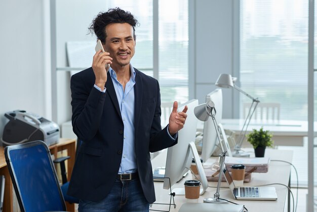 Middellange lengte van Aziatische ondernemer praten aan de telefoon in zijn lichte kantoor
