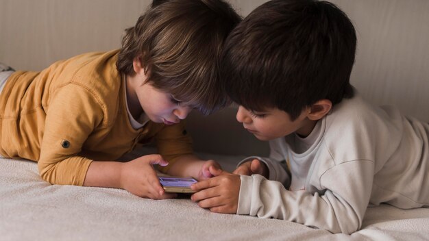 Middellange shot kinderen in bed met smartphone