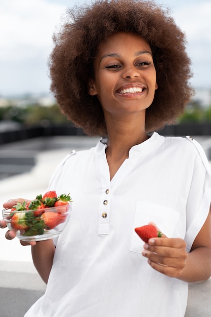 Gratis foto middellange shot smileyvrouw die aardbeien eet