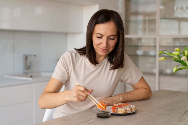 Gratis foto middellange shot vrouw die thuis sushi eet