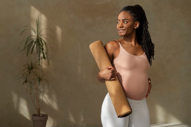Gratis foto middellange shot zwangere vrouw met yogamat