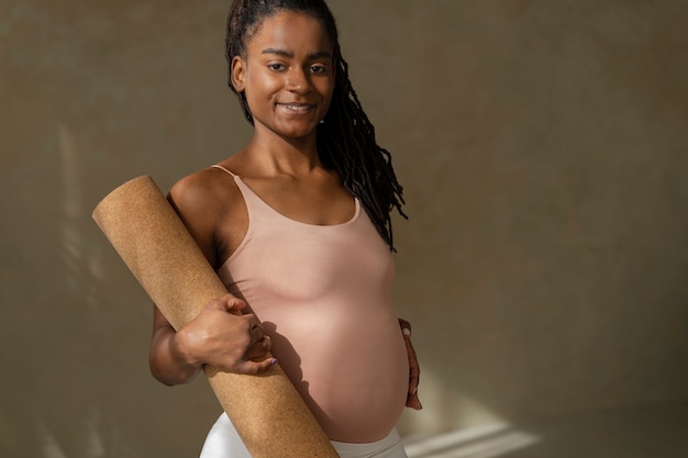 Gratis foto middellange shot zwangere vrouw met yogamat