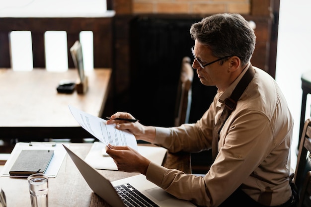 Midden volwassen eigenaar van een klein bedrijf die rapporten analyseert terwijl hij aan papierwerk in een pub werkt