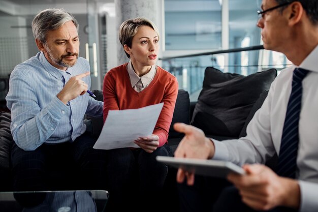 Midden volwassen stel en hun financieel adviseur bespreken papierwerk tijdens de vergadering