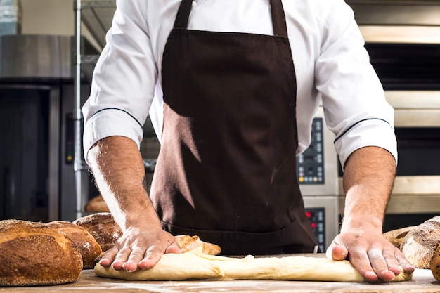 Midsection van een mannelijke bakker die het deeg in de bakkerij kneden