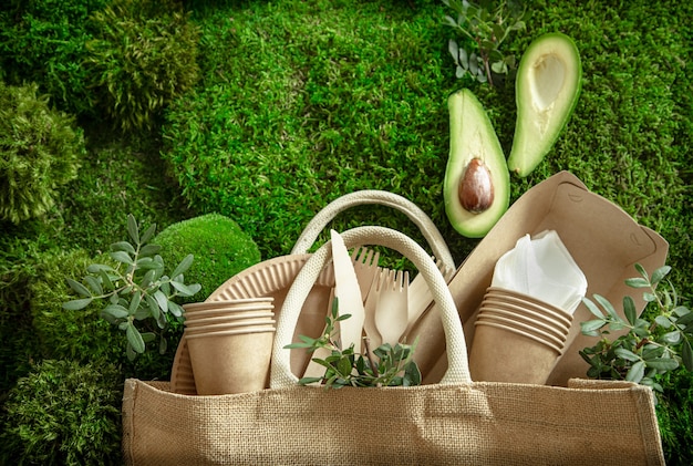 Milieuvriendelijk, wegwerp- en recyclebaar serviesgoed. Papieren voedseldozen, borden en bestek van maïszetmeel op een achtergrond van groen gras.