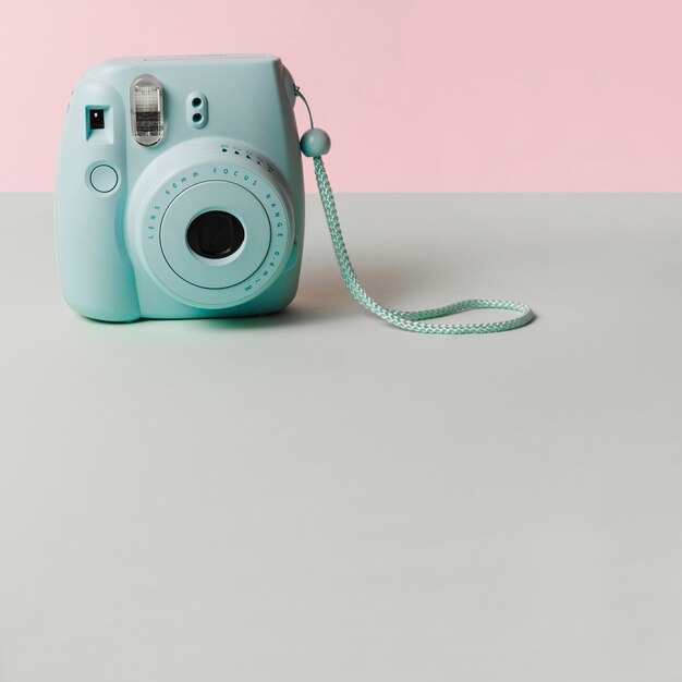 Mini blauwe onmiddellijke camera op grijs bureau tegen roze achtergrond