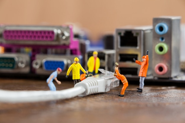 Gratis foto miniatuur ingenieur en werknemer plug-in lan-kabel op de computer