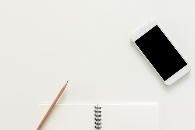 Minimale werkruimte - creatieve platte lay-out van werkruimte bureau met schetsboek en mobiele telefoon met leeg scherm op kopie ruimte witte achtergrond. bovenaanzicht, plat legfotografie.