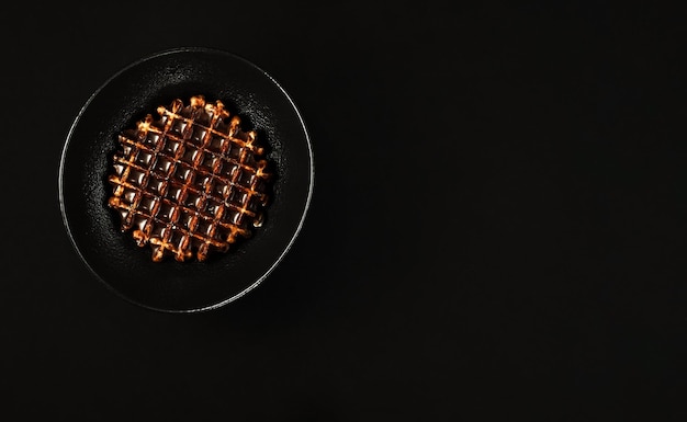 Minimalistisch ontbijtidee in zwarte kleur Belgische wafels met donkere chocolade op een zwarte plaat dessertidee voor tafelsetting Plat lag Zwarte achtergrond bovenaanzicht met kopieerruimte