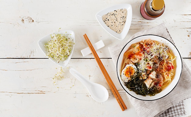 Miso Ramen Aziatische noedels met koolkimchi, zeewier, ei, paddestoelen en kaastofu in kom op witte houten lijst.