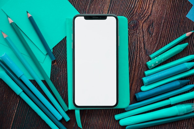 Mobiele telefoon met wit scherm op dagboek in de buurt van schilderen kleuren over houten tafel