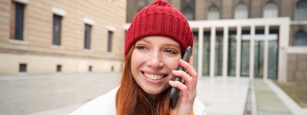 Gratis foto mobiele verbinding en mensen concept gelukkige roodharige vrouw in hoed praat over het maken van mobiele telefoons