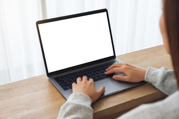 Mockup-afbeelding van een vrouw die een laptop gebruikt en typt met een leeg wit desktopscherm op houten tafel