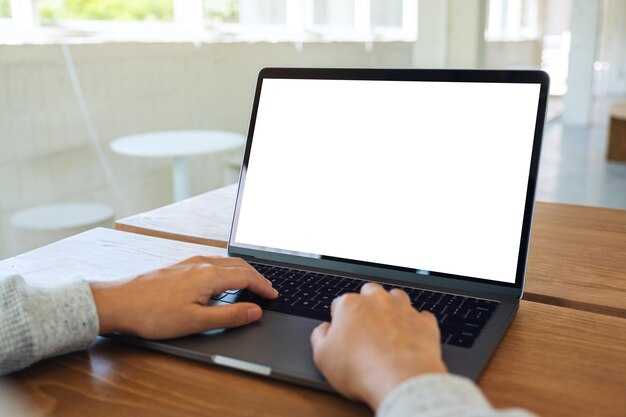 Mockup-afbeelding van een vrouw die gebruikt en typt op het toetsenbord van een laptopcomputer met een leeg wit desktopscherm op houten tafel