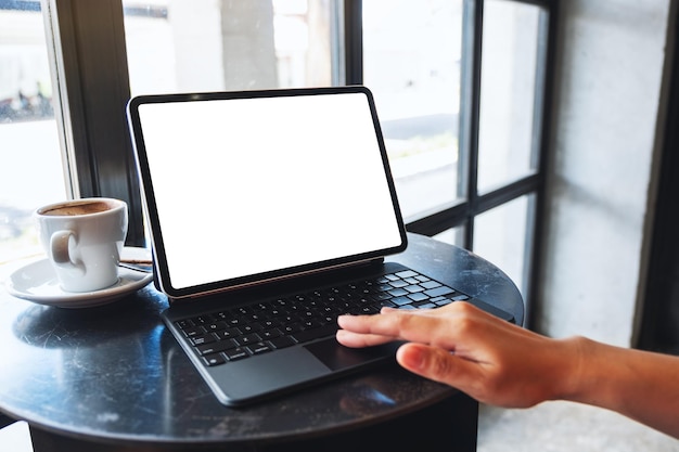 Mockup-afbeelding van een vrouw die het touchpad van een tablet aanraakt met een leeg wit bureaubladscherm als een computer-pc met een koffiekopje op tafel Premium Foto