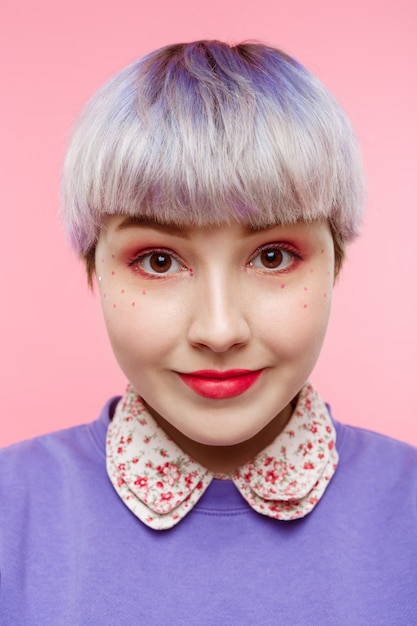 Gratis foto mode close-up portret van smling mooi dollish meisje met kort licht violet haar draagt lila trui over roze muur