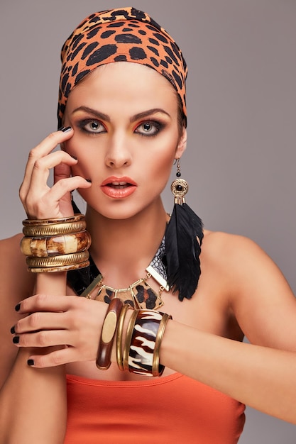 Mode-concept. Mooie kaukasische vrouw met make-up die kleurrijke sjaal op hoofd en toebehoren draagt. Geïsoleerd op grijze achtergrond.