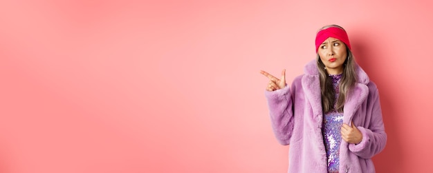 Gratis foto mode en winkelconcept sceptische aziatische vrouw van middelbare leeftijd in paarse bontjas die kijkt en wijst