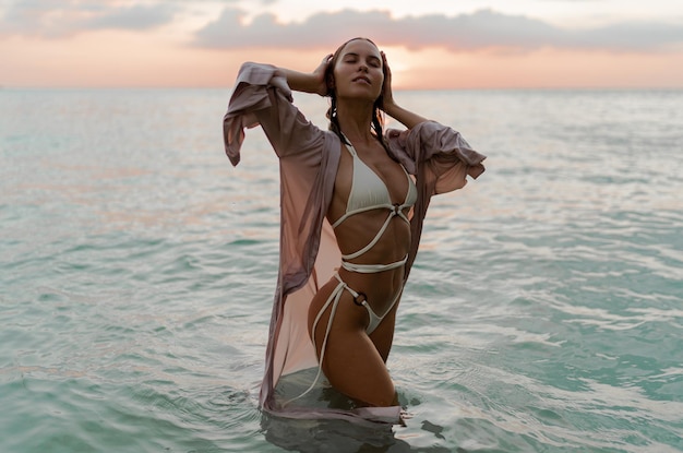 Gratis foto mode foto van verleidelijke model met perfect lichaam poseren op het tropische strand. zonsondergang collots.