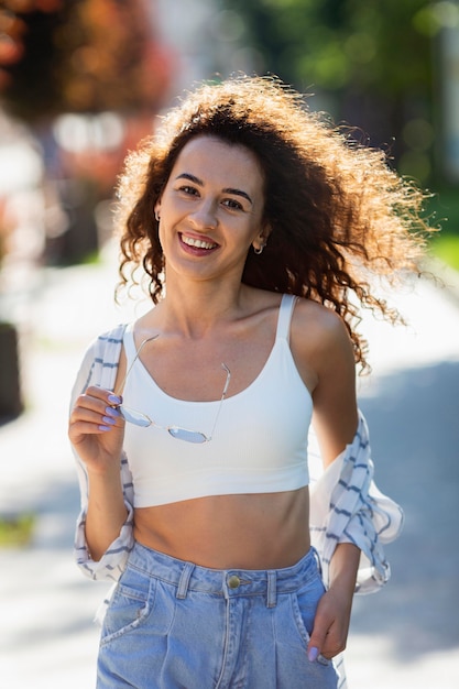 Gratis foto mode jonge vrouw poseren buitenshuis terwijl ze haar zonnebril vasthoudt