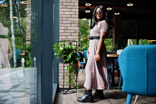 Mode portret van Afro-Amerikaanse vrouw in lange jurk laarzen en zonnebril indoor