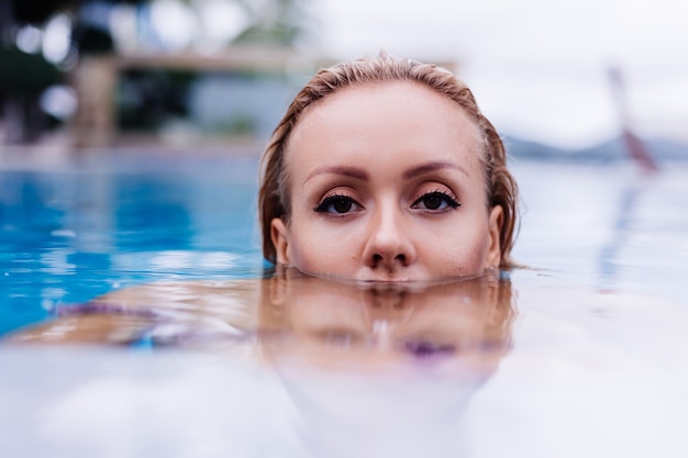 Mode portret van blanke vrouw in bikini in blauw zwembad op vakantie bij dag natuurlijk licht