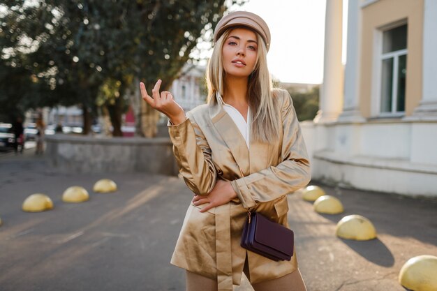 Mode portret van elegante blonde vrouw in lederen hoed en casual beige jas. Live; y vrouwelijke poseren buiten. zonsondergang licht. Herfst look.