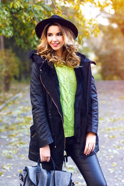 Gratis foto mode portret van mooie jonge blonde lachende vrouw trendy jas, vintage hoed en neon trui dragen, poseren op platteland park in mooie zonnige herfst herfstdag.