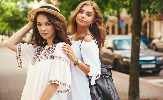 Mode portret van twee jonge stijlvolle hippie brunette en blonde vrouwen modellen in zonnige zomerdag in witte hipster kleding poseren. Geen make-up