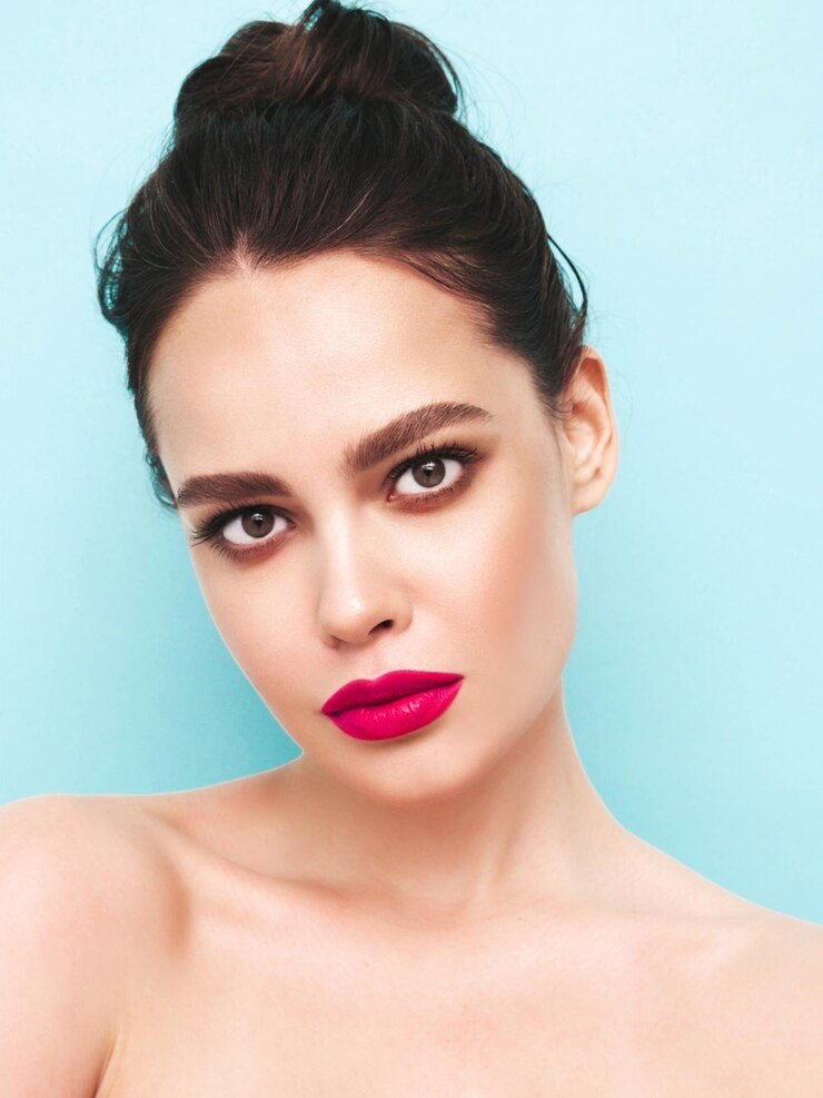 Gratis Foto mode schoonheid portret van jonge brunette vrouw met stijlvolle avond make-up en perfecte schone huid sexy model met haar in een broodje poseren in studio in de buurt van blauwe muur met roze heldere natuurlijke lippen