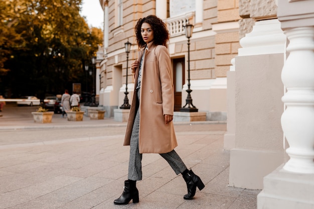 Mode volledige lengte afbeelding van elegante zwarte vrouw in stijlvolle luxe beige jas en fluwelen trui