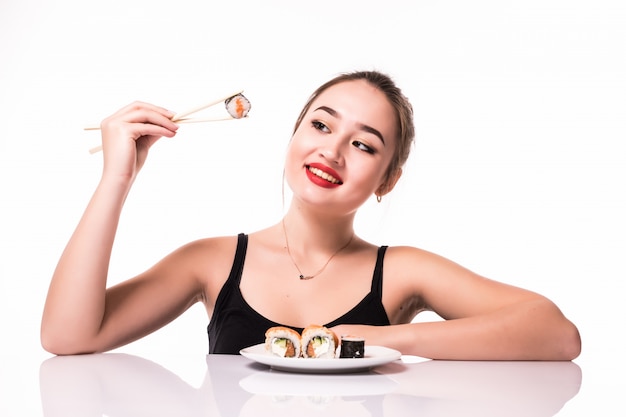 Model Aziaat kijkt met bescheiden kapsel zit op de lijst eet sushibroodjes glimlachen geïsoleerd op wit