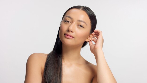 Model van gemengd ras raakt haar haar aan en kijkt naar de camera gloeiende natuurlijke ideale huid