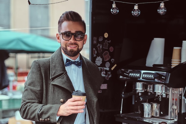 Moderne lachende man in zonnebril drinkt koffie terwijl hij buiten in de coffeeshop staat.